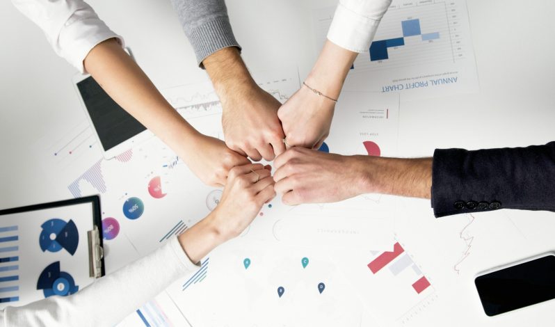 Free Colleagues celebrate success with a fist bump over financial charts depicting teamwork and unity. Stock Photo